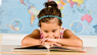 ילדה עם קשת תכולה בשיערה נשענת קדימה וקוראת בספר (צילום: istockphoto)