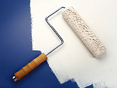 רולר לצביעת קירות מונח עם צבע לבן על משטח כחול