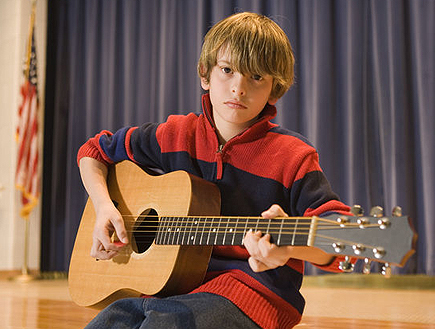 ילד יושב על במה ומנגן בגיטרה (צילום: jupiter images)