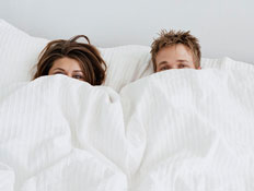 זוג מציץ מבעד לשמיכה על מיטה לבנה (צילום: jupiter images)