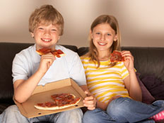 נער ונערה מחייכים ואוכלים פיצה על ספה