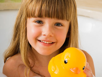 ילדה עם פוני באמבטית קצף מחזיקה ברווז צהוב ומחייכת