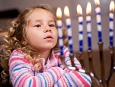 ילדה עם פסים מסתכלת על נרות דלוקים בחנוכיה (צילום: istockphoto)