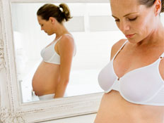 בחורה בהריון בתחתונים וחזייה לבנים עומדת ליד מראה ומביטה למטה (צילום: jupiter images)