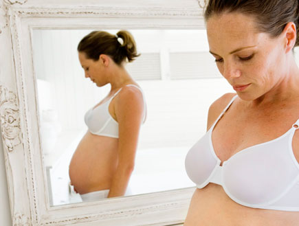 בחורה בהריון בתחתונים וחזייה לבנים עומדת ליד מראה ומביטה למטה (צילום: jupiter images)