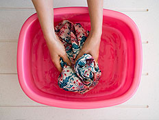 ידיים מכבסות בגד בתוך קערת מים ורודה