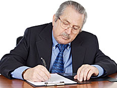 איש מבוגר יושב בחליפה ועניבה וכותב בעט על דף (צילום: Gelpi, Istock)
