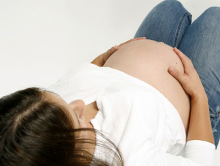 אישה בהריון בג'ינס שוכבת ומחזיקה את הבטן (צילום: istockphoto)