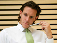 גבר בעניבה ירוקה עם עט יושב לשולחן וחושב (צילום: jupiter images)