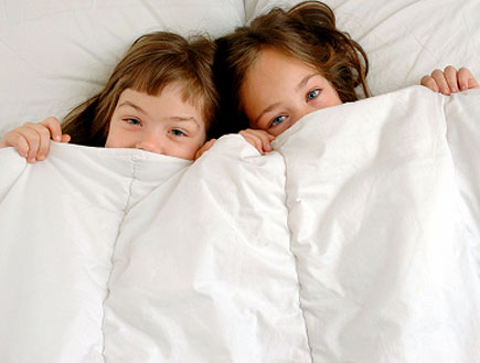 שתי ילדות מציצות משמיכת פוך לבנה במיטה (צילום: Maica, Istock)