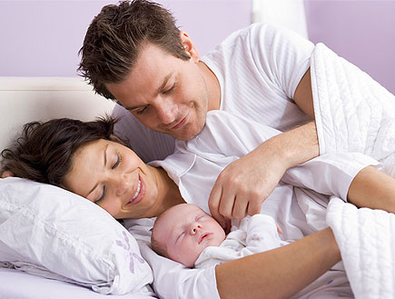 זוג צעיר מחבק תינוק על מיטה בחדר סגול