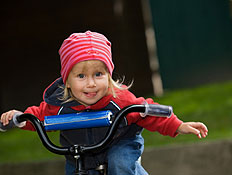 ילדה בכובע ורוד על אופניים מוציאה לשון (צילום: istockphoto)