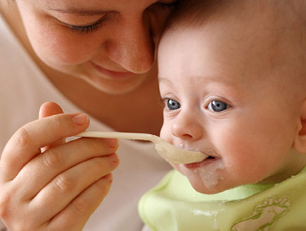 אישה מאכילה בכפית תינוק מחייך לבוש ירוק (צילום: Damir Cudic, Istock)