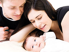 זוג בשחור מביט בעונג על תינוקם בלבן על מיטה (צילום: istockphoto)