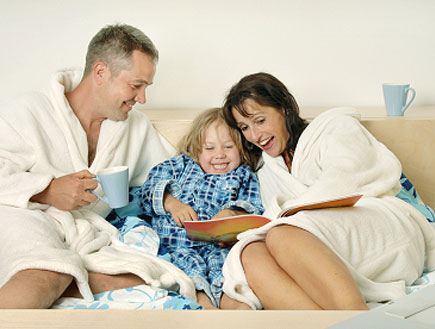 הורים בחלוק קוראים ספר במיטה עם בתם (צילום: Maartje van Caspel, Istock)
