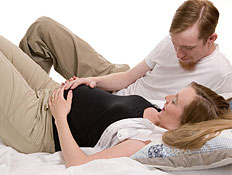 גבר מניח ידו על בטן של אישה בהריון בשחור על מיטה (צילום: Mark Hayes, Istock)