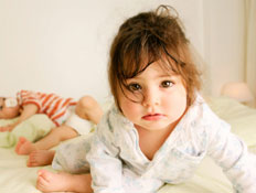 פעוטה על מיטה מביטה למצלמה וברקע ילד בפסים שוכב (צילום: Weekend Images Inc., Istock)