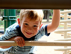 יום כיף: ילד מציץ מבעד לברזלים של מתקנים בגן שעשוע
