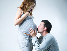 גבר על ברכיו מנשק בטן של אישה בהריון מחיייכת (צילום: piskunov, Istock)