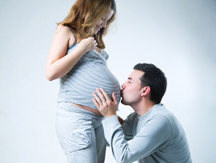 גבר על ברכיו מנשק בטן של אישה בהריון מחיייכת (צילום: piskunov, Istock)