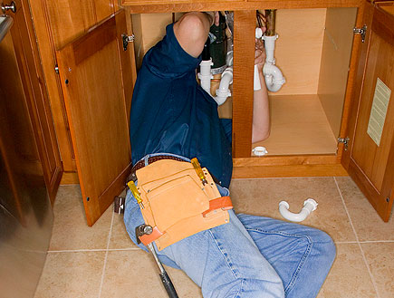 שרברב בג'ינס שוכב מתחת ומתקן כיור עם כלים (צילום: jupiter images)
