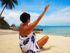 אישה יושבת בחוף ים, מרימה ידיים לאוויר (צילום: Shutterstock)