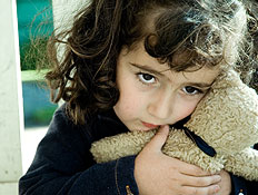 ילדה מפוחדת בשחור מחבקת דובי ליד גדר (צילום: istockphoto)