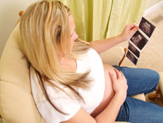 אישה בהריון מסתכלת בתמונות אולטרסאונד על כורסא (צילום: istockphoto)