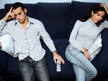 זוג מיואש על ספה מחזיקים את הראש וביניהם שלט (צילום: istockphoto)