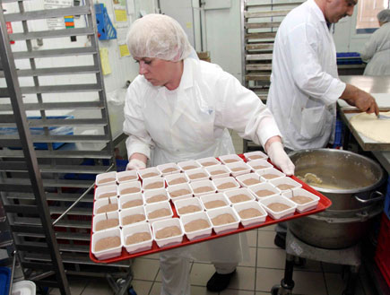 אישה אוחזת מגש עמוס קופסאות במפעל לאוכל של מטוסים (צילום: עדי רם)