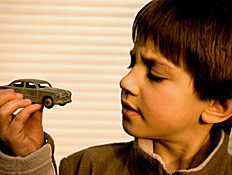 ילד בחולצה חומה מסתכל אל מכונית צעצוע