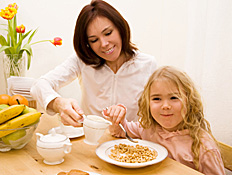 ילדה בלונדינית אוכלת קורנפלקס ליד אמה