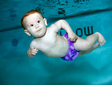 תינוק עם בגד ים סגול צולל לבדו בבריכת שחייה