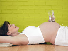 אישה בהריון נחה על הגב ועל ביטנה כוס זכוכית (צילום: jupiter images)