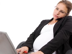 אישה בהריון לבושה בחליפה מדברת בטלפון מול מחשב (צילום: istockphoto)