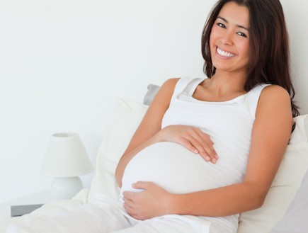 אישה בהריון מחייכת מניחה ידיים על הבטן (צילום: ThinkStock)