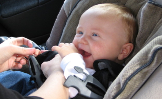 ידיים חוגרות בכיסא ברכב תינוק מחייך עם אצבע בפה (צילום: istockphoto)