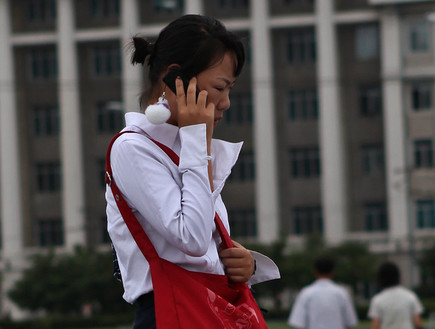 אישה בקוריאה הצפונית מדברת בטלפון סלולרי (צילום: Roman Harak, Flickr)