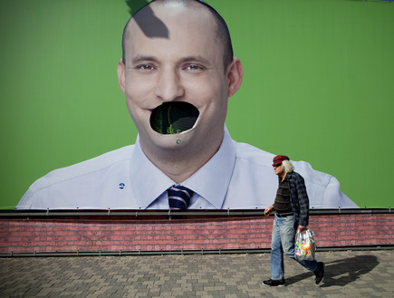 איש הולך מול שלט בחירות של נפתלי בנט שהושחת (צילום: ap)