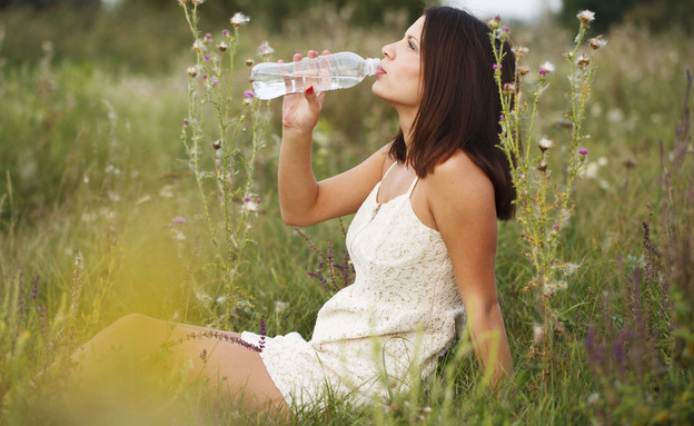 אישה בשדה שותה מבקבוק מים (אילוסטרציה: mikanaka, Thinkstock)