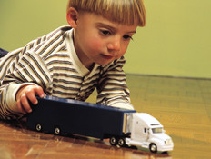 ילד עם פסים שוכב על רצפה ומשחק עם משאית צעצוע