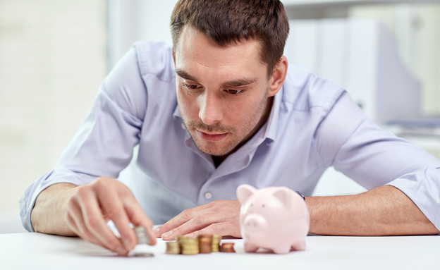 איש עסקים סופר מטבעות ליד קופת חיסכון (אילוסטרציה: Shutterstock)