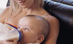 אישה מאכילה תינוק בבקבוק על ספה ומאחוריה גבר מסתכל (צילום: jupiter images)