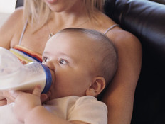 אישה מאכילה תינוק בבקבוק על ספה ומאחוריה גבר מסתכל (צילום: jupiter images)