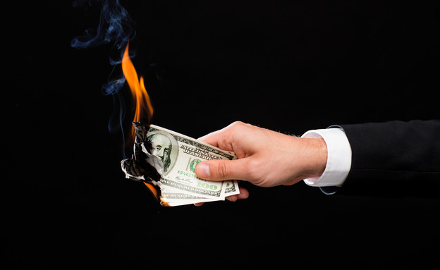 יד מחזיקה שטרות דולר שנשרפים (אילוסטרציה: Shutterstock)