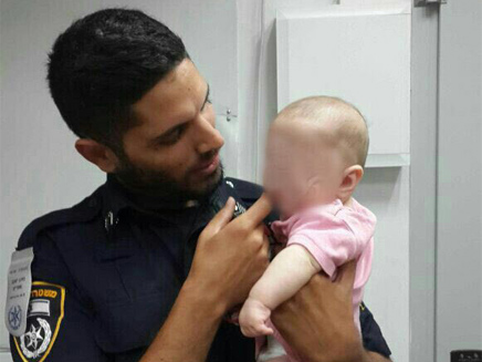 התינוקת עם אחד השוטרים שמצאו אותה (צילום: חטיבת דוברות המשטרה)
