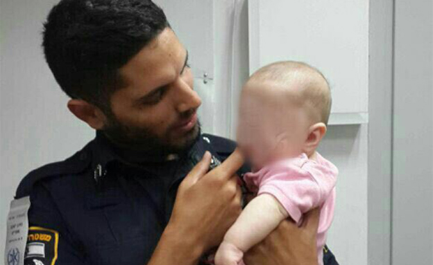 התינוקת עם אחד השוטרים שמצאו אותה (צילום: חטיבת דוברות המשטרה)