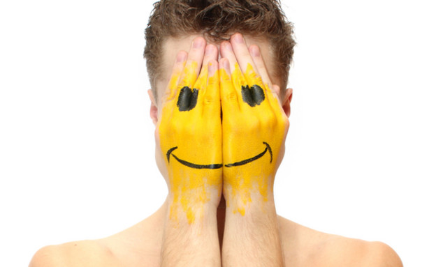 גבר מסתיר את פניו בידיו עליהן מצויר סמיילי (צילום: ShutterStock)