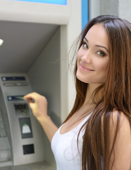 אישה מחייכת מוציאה כסף מכספומט (אילוסטרציה: Shutterstock)