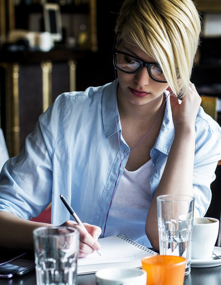 אישה יושבת וכותבת בבית קפה (אילוסטרציה: Shutterstock)